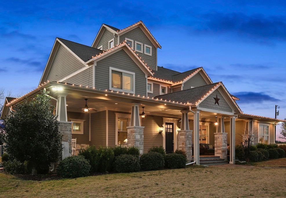 Gray house with porch, Christmas lights, stone columns, and a star decoration at dusk.