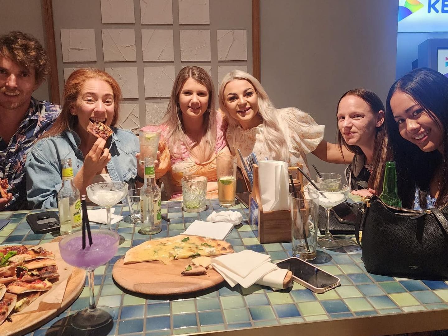 A group of people are sitting at a table with pizza and drinks.