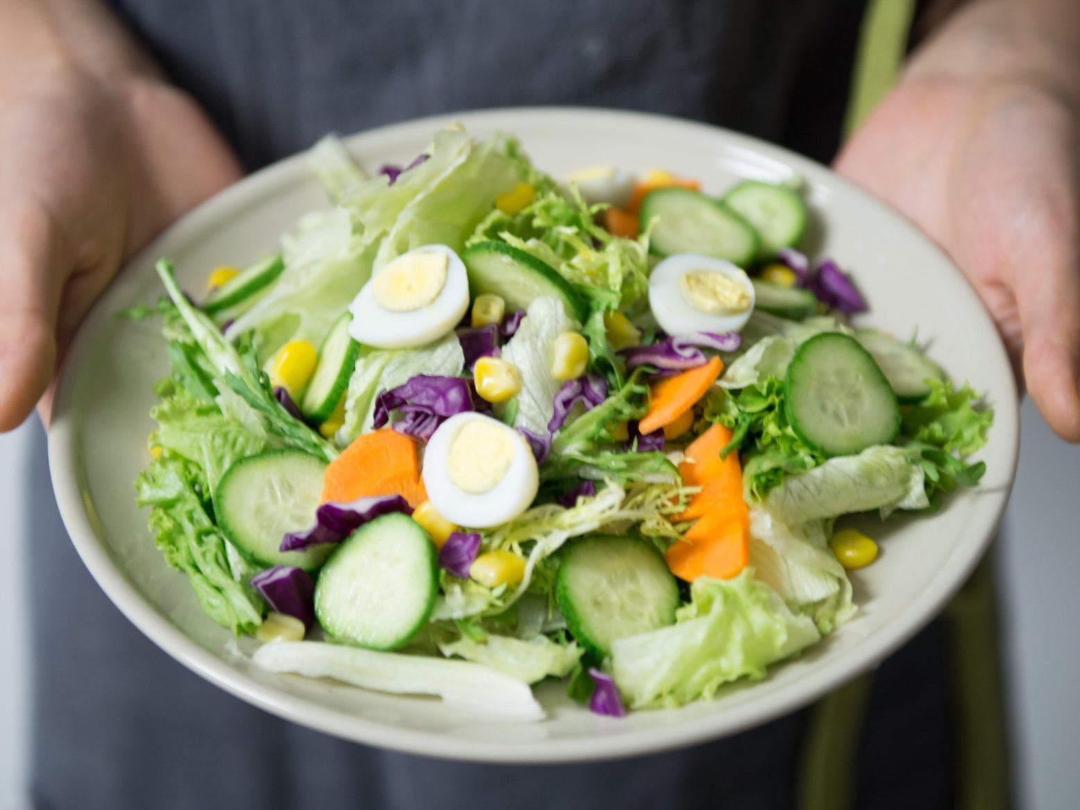 A person is holding a plate of salad with eggs and vegetables.