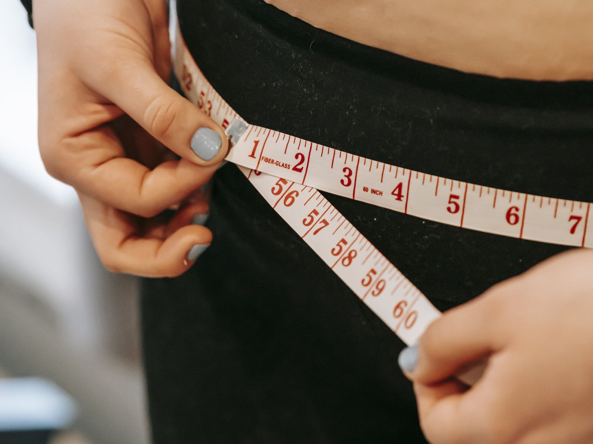 A woman is measuring her waist with a tape measure.