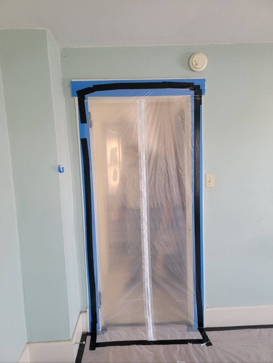 Doorway covered in plastic, taped off for painting, in a room with blue walls.