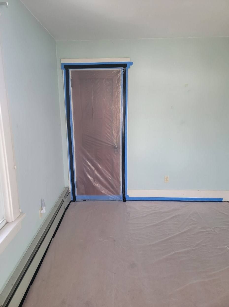 A room with blue walls, a door covered in plastic, and the floor protected; ready for painting.