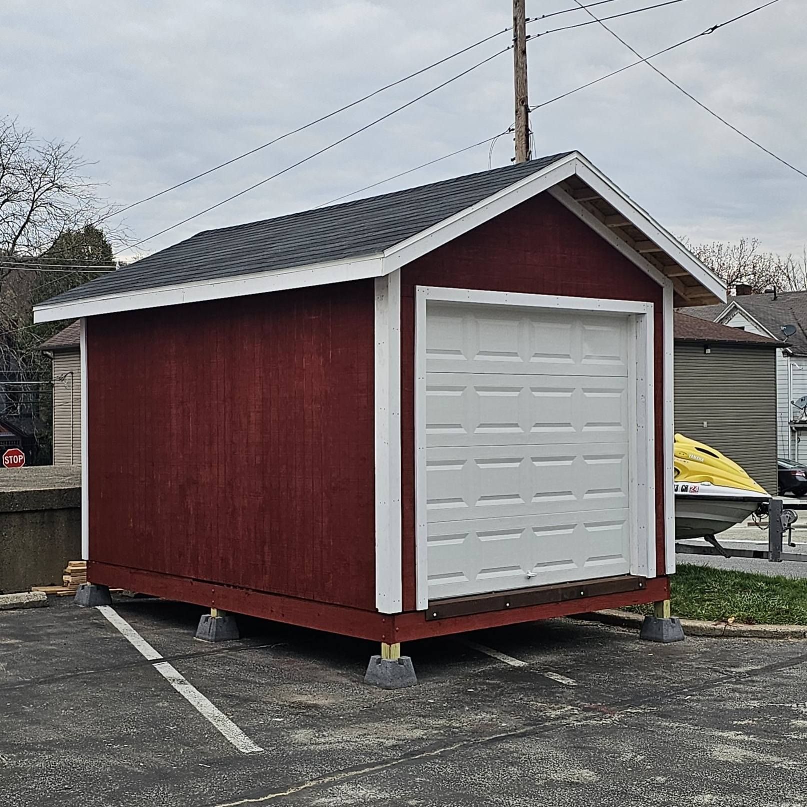 Red shed with white door, built on concrete blocks, in a parking lot.
