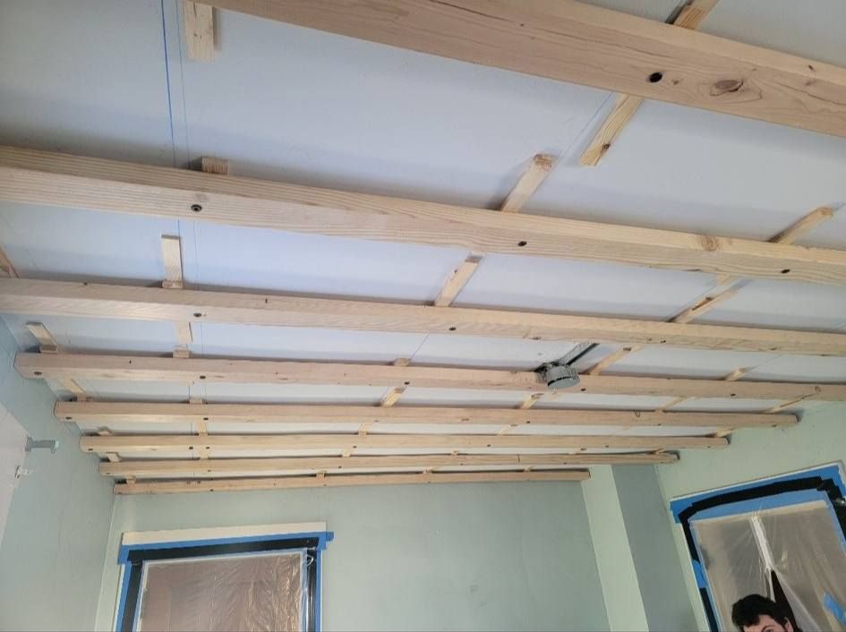 Wooden beams and insulation installed on a ceiling in a room, windows visible.