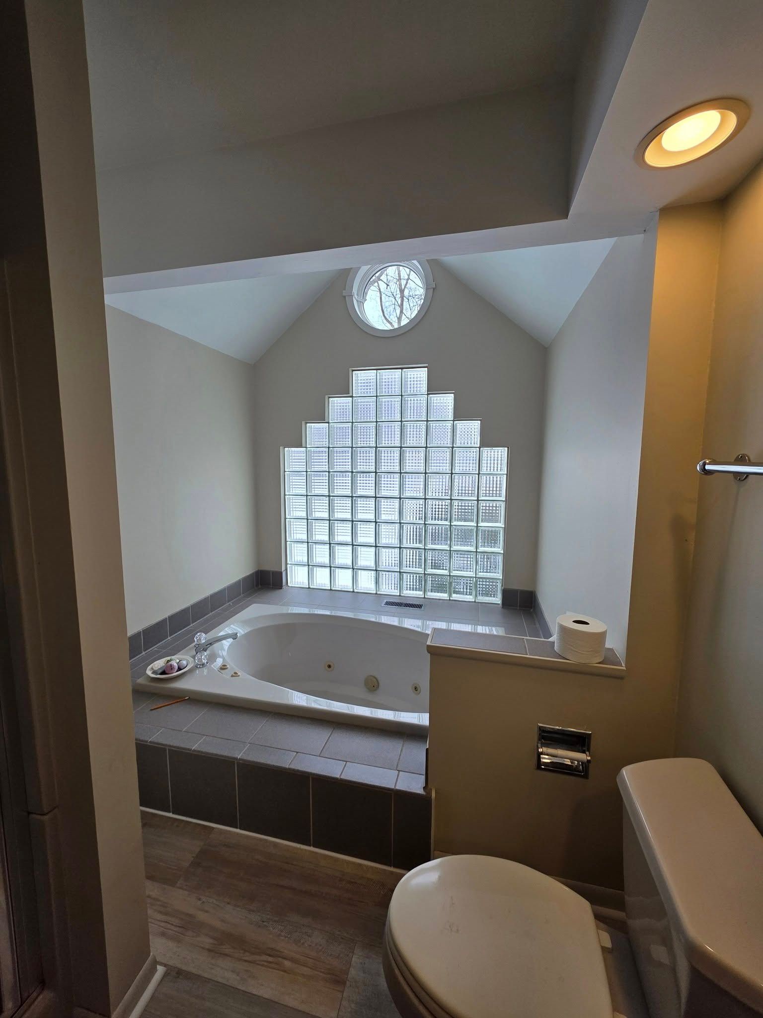Bathroom with a jacuzzi and glass block window. The toilet is in the foreground.