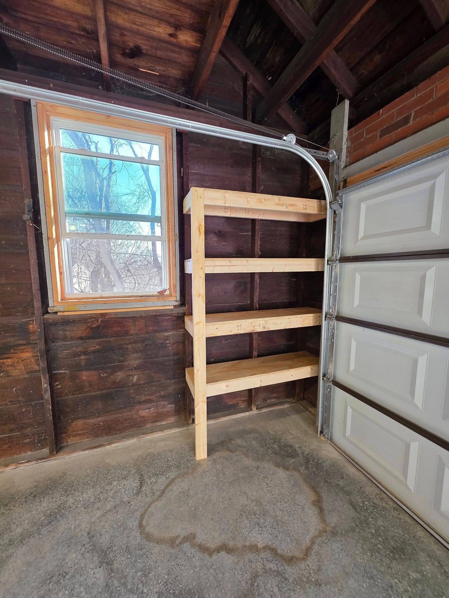 Wooden shelves beside a closed garage door, inside a garage with a window.