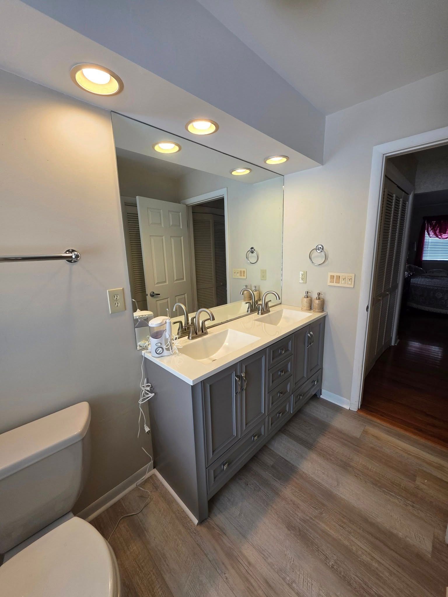 Bathroom with double vanity, mirror, toilet, and wood-look floor; gray and white color scheme.