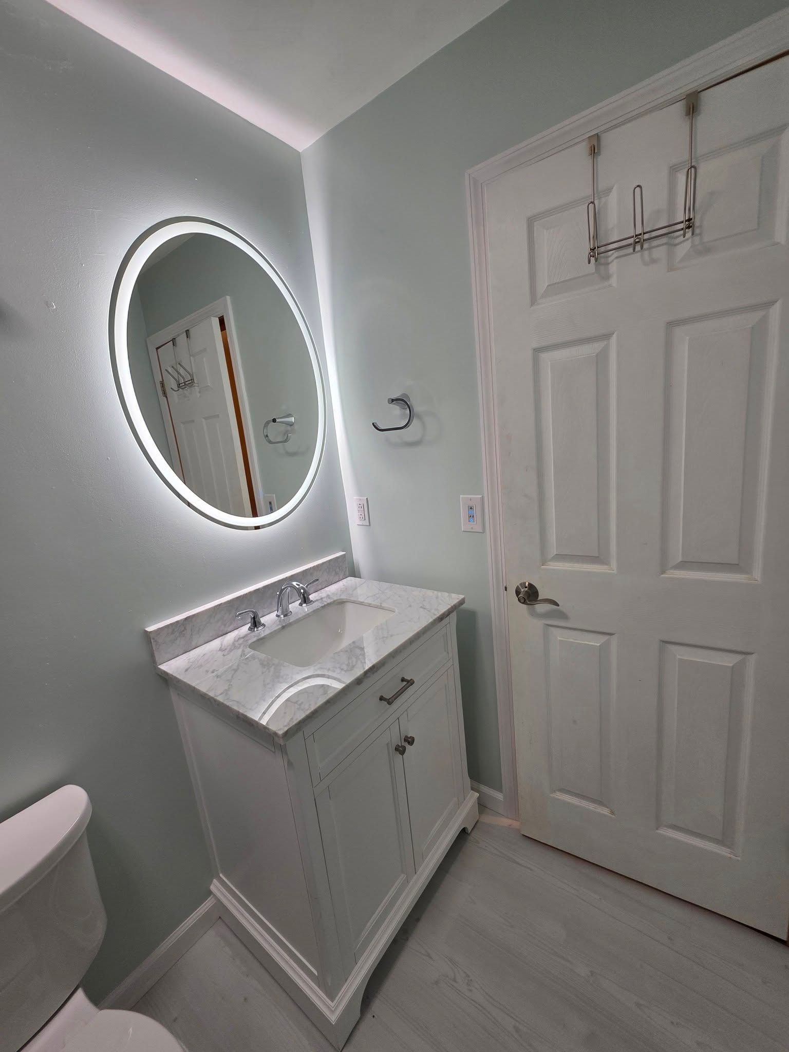 Bathroom with a lighted mirror, white vanity, and a closed door.
