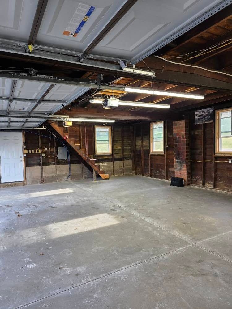 Empty garage with wooden walls, a staircase, and overhead lights.