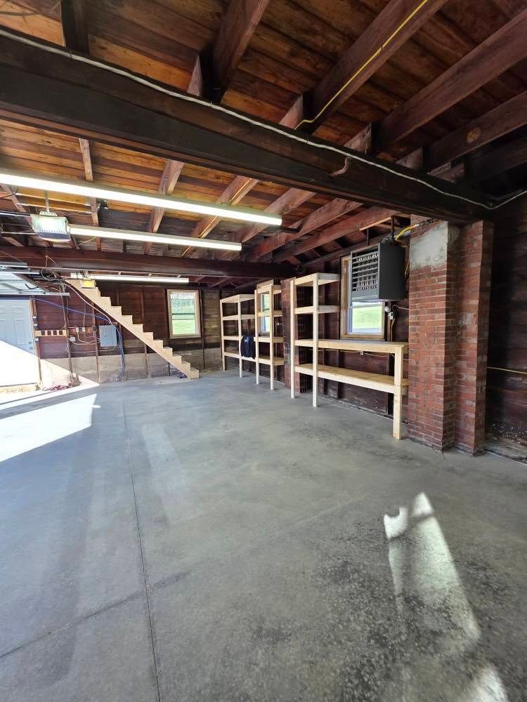 Empty garage with concrete floor, wooden shelving, and stairs leading up.
