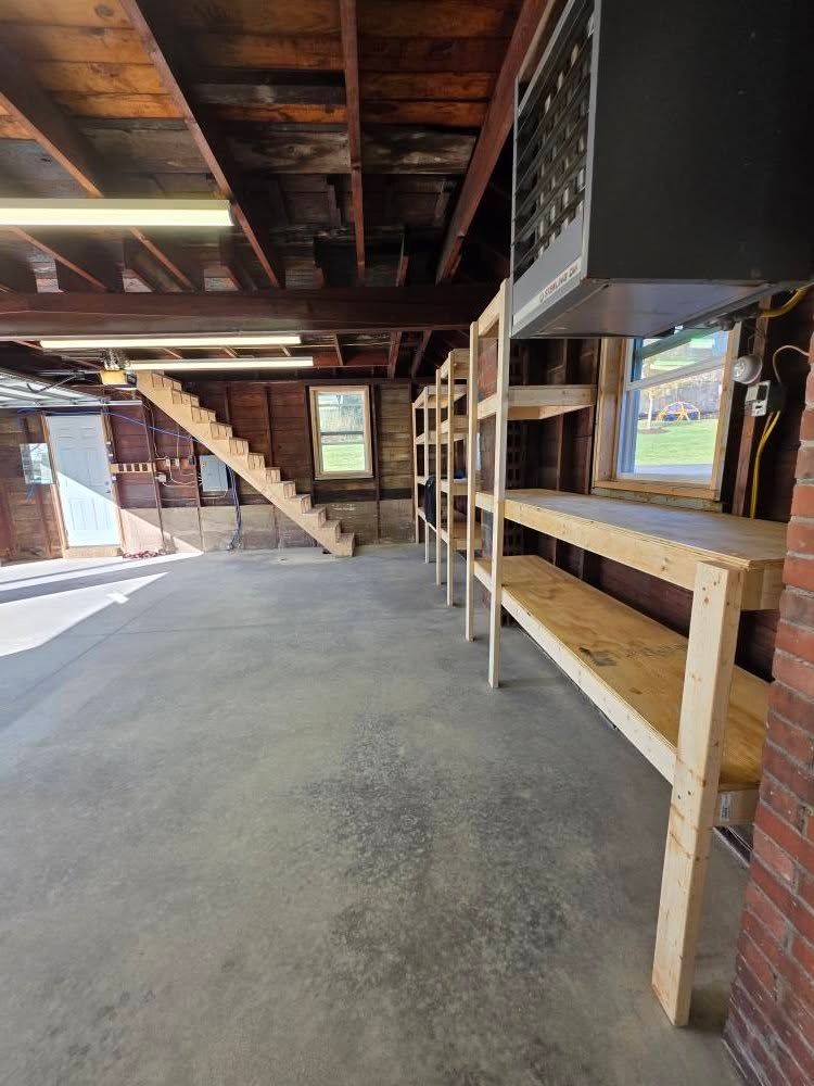 Garage interior with concrete floor, wooden shelving, stairs, and a door.