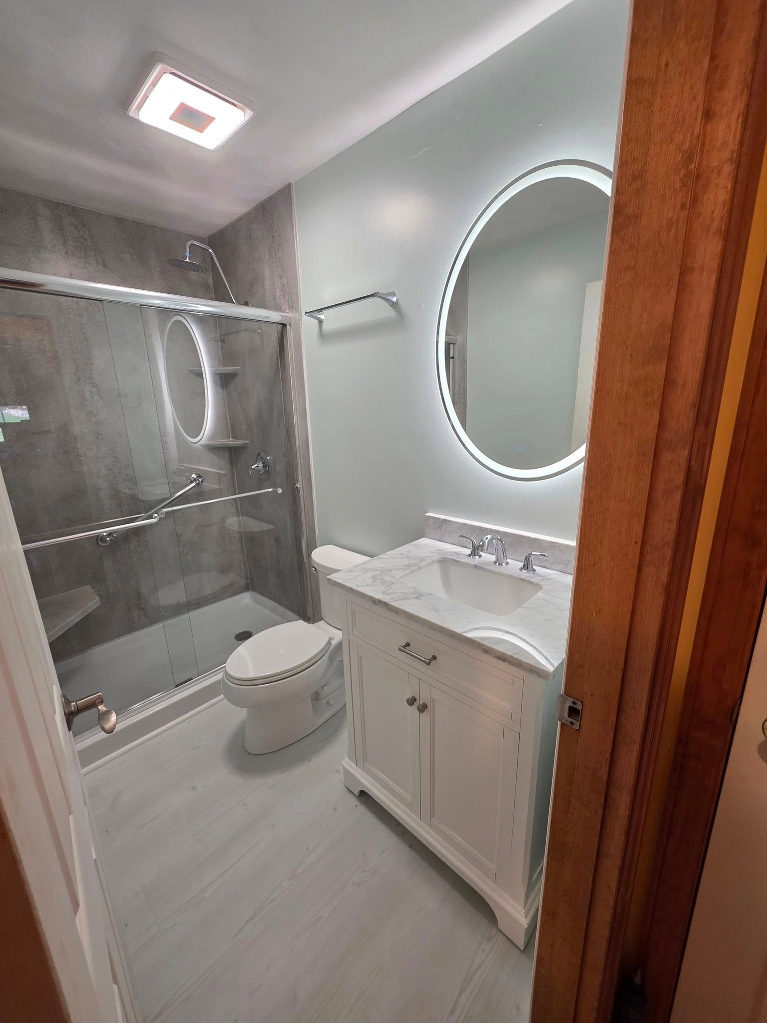 Modern bathroom with gray tile shower, white vanity, and round mirror.