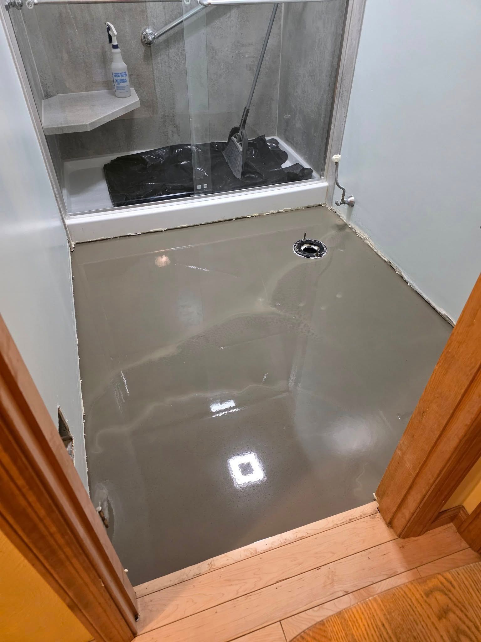 Gray floor freshly poured, leading to a shower with glass doors and a black mat.