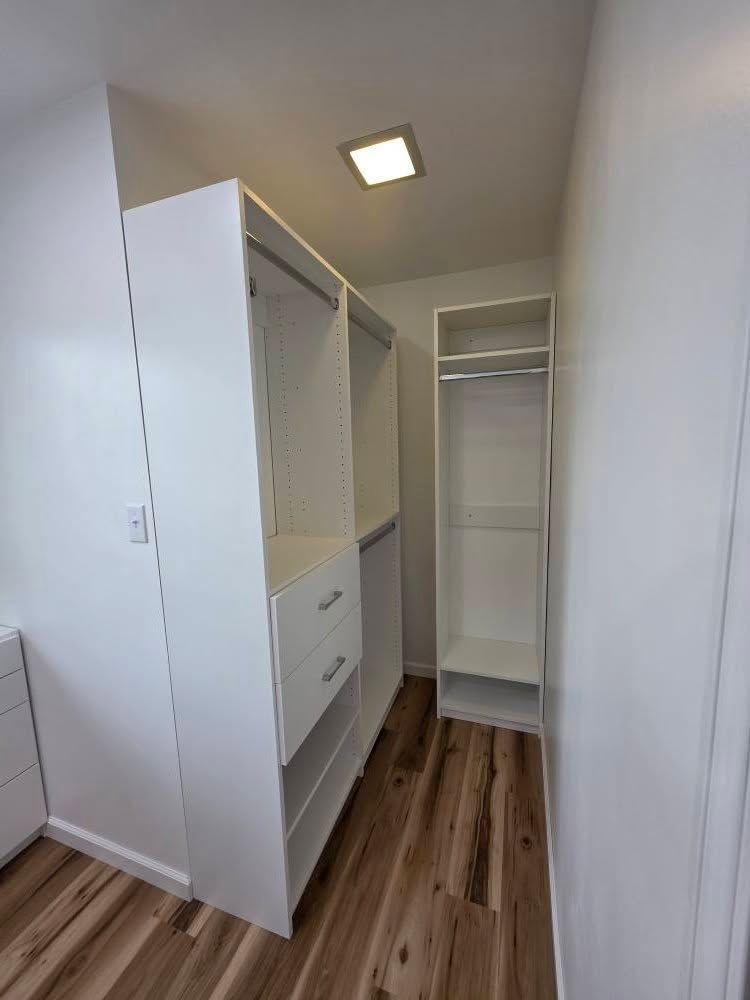 White closet organizers in a small room with wood-look flooring; clothes hanging rods, drawers, and shelves.