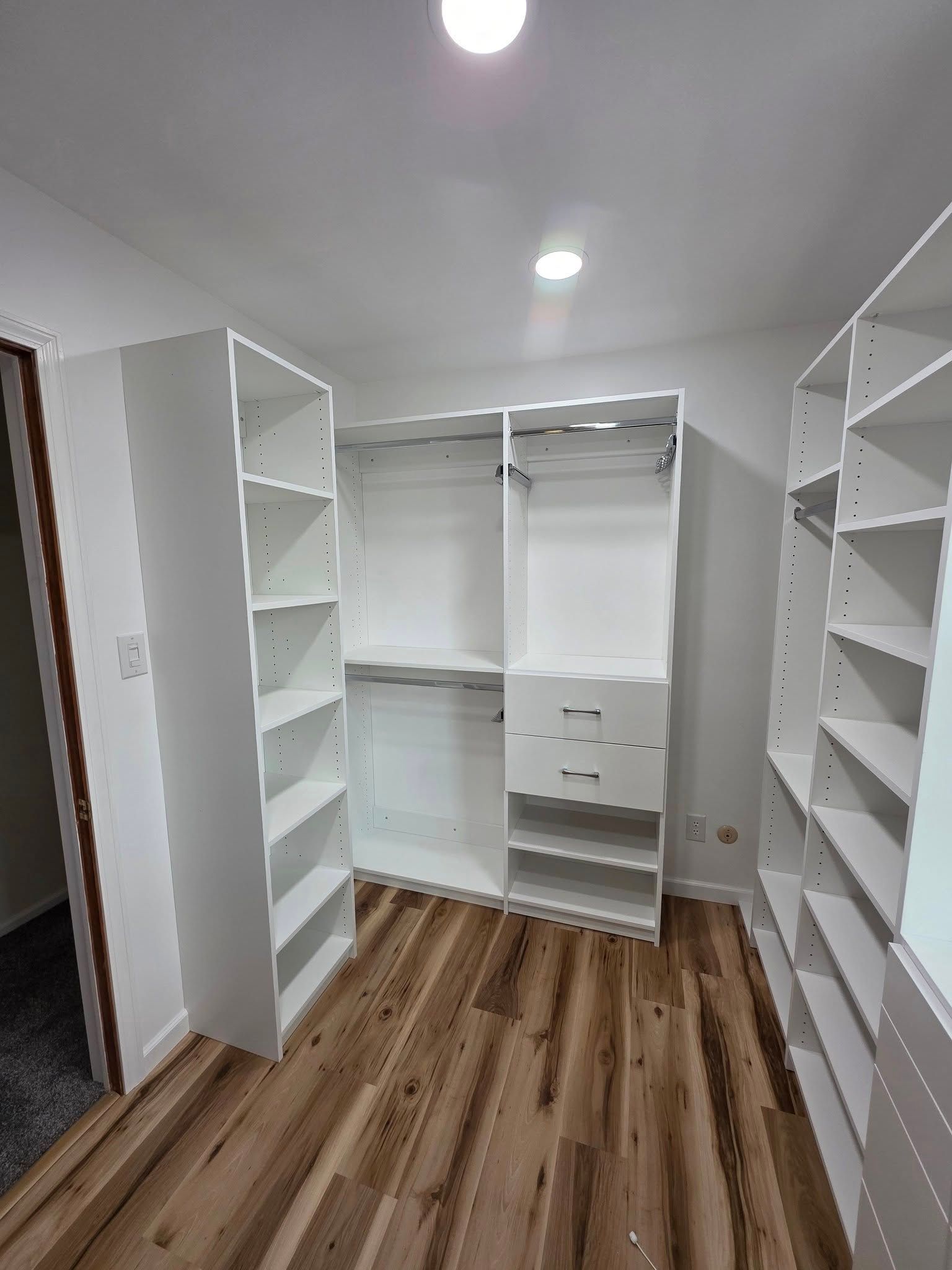 White custom closet with shelves and rods, in a room with wood flooring.