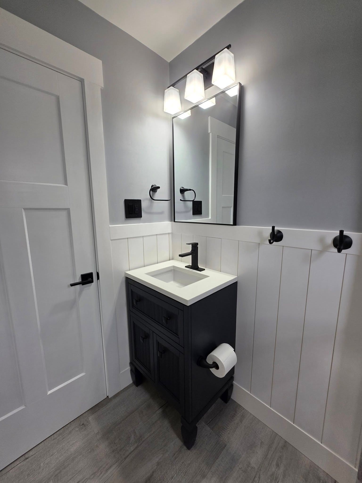 Bathroom with dark blue vanity, white beadboard, black fixtures, and a mirror.
