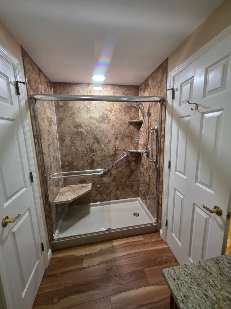 Bathroom with a shower featuring a bench, grab bar, and textured wall. Wood-look flooring, two doors.