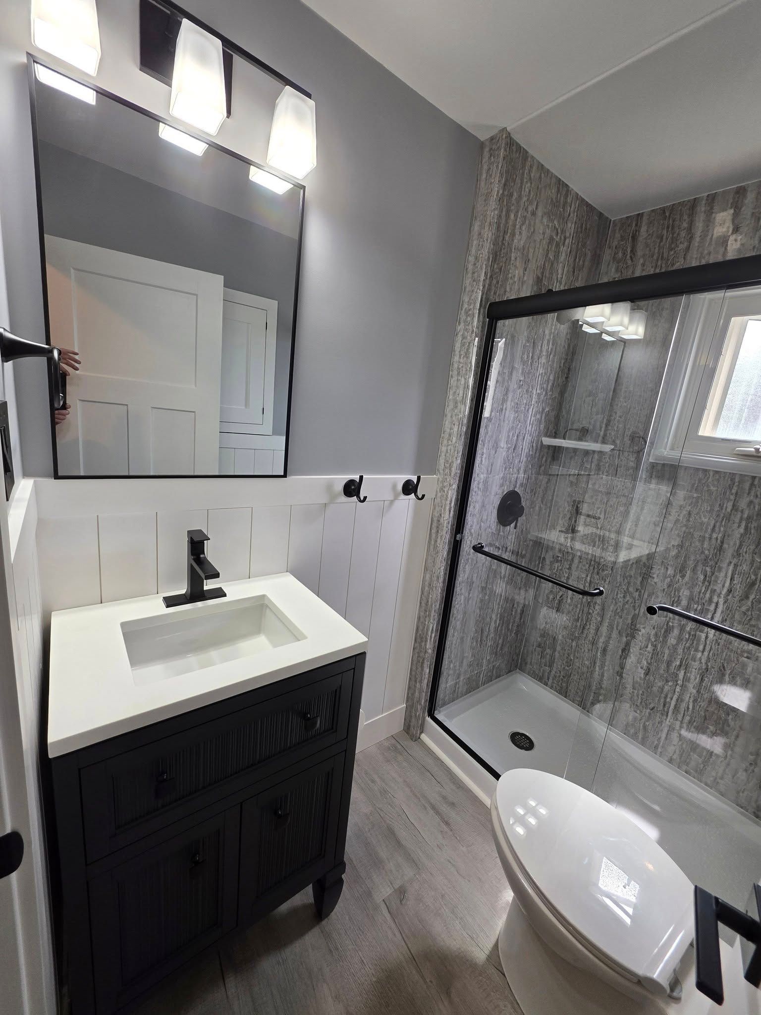 Modern bathroom with black vanity, gray walls, tiled shower, and a toilet.