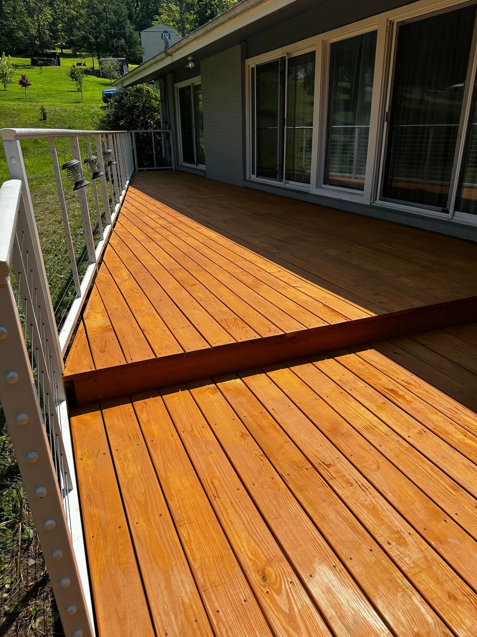 Wooden deck, stained orange, with white railing, next to a house with glass doors.