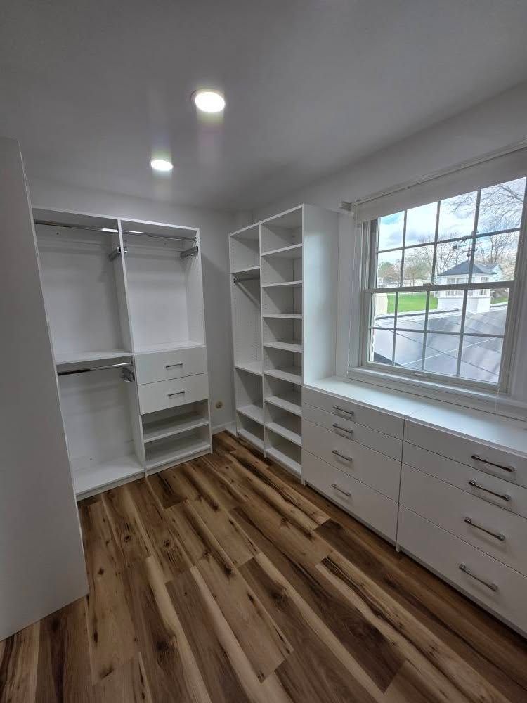 White closet organization system in a room with wood flooring and a window.