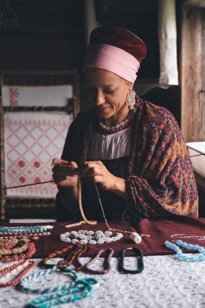 A woman is sitting at a table making necklaces.