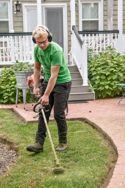 A man is using a lawn mower to cut the grass in front of a house.