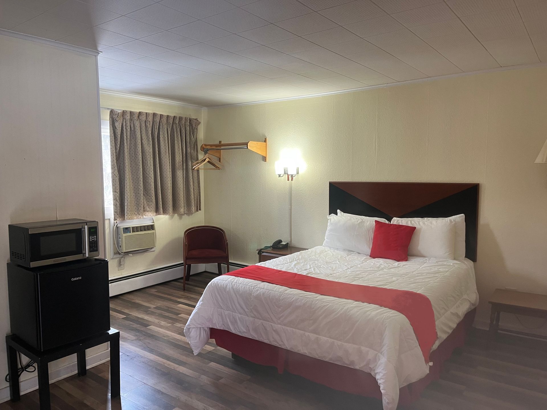 A hotel room with a bed , chair , microwave and refrigerator.