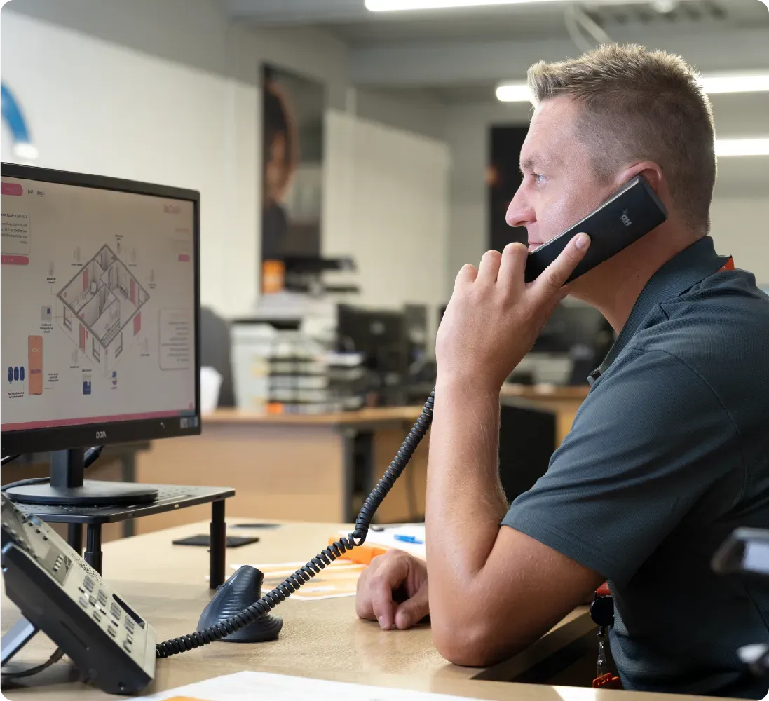 Man on phone at desk, looking at a computer screen displaying a diagram. Office setting.