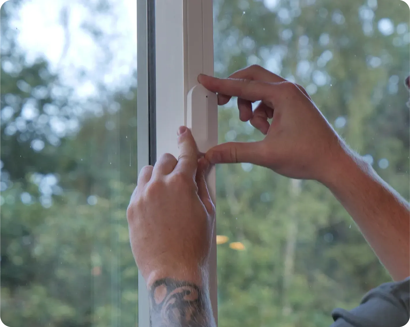 Person's hands adjusting a white window seal next to glass window with trees visible in the background.