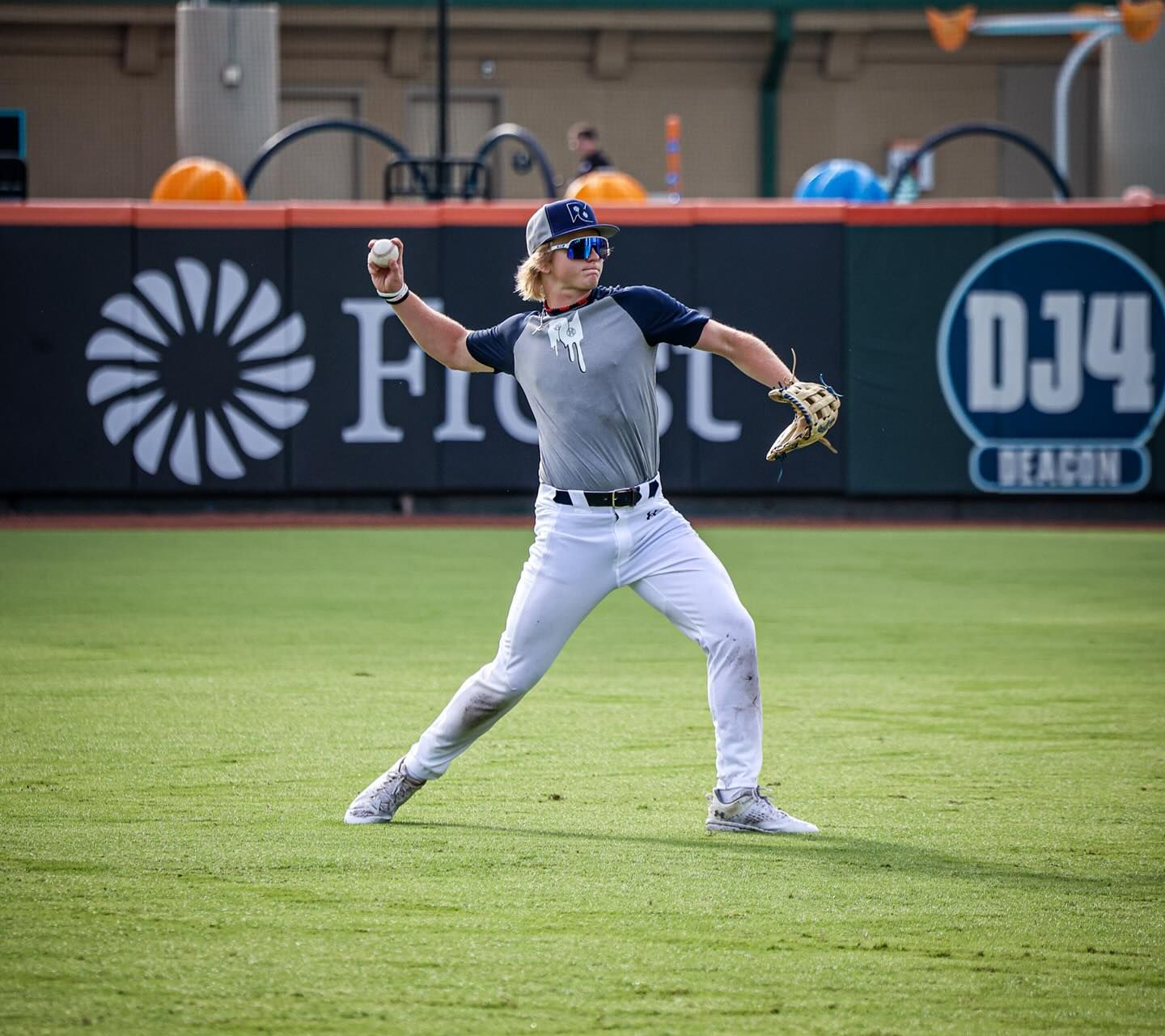 Baseball player in gray uniform throws a ball on a green field.