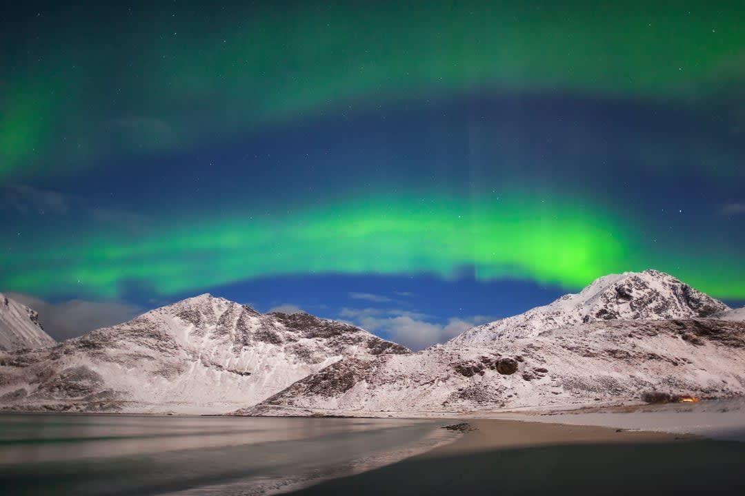 The aurora borealis is shining over a snowy mountain range.