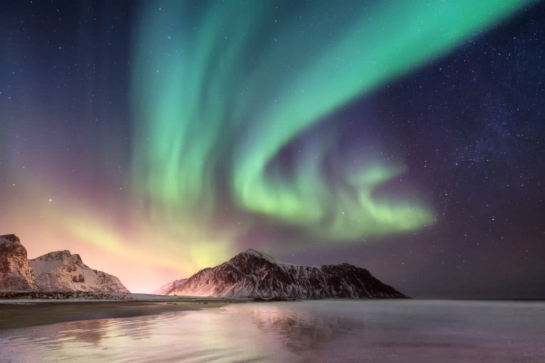 The aurora borealis is dancing in the night sky over a beach.