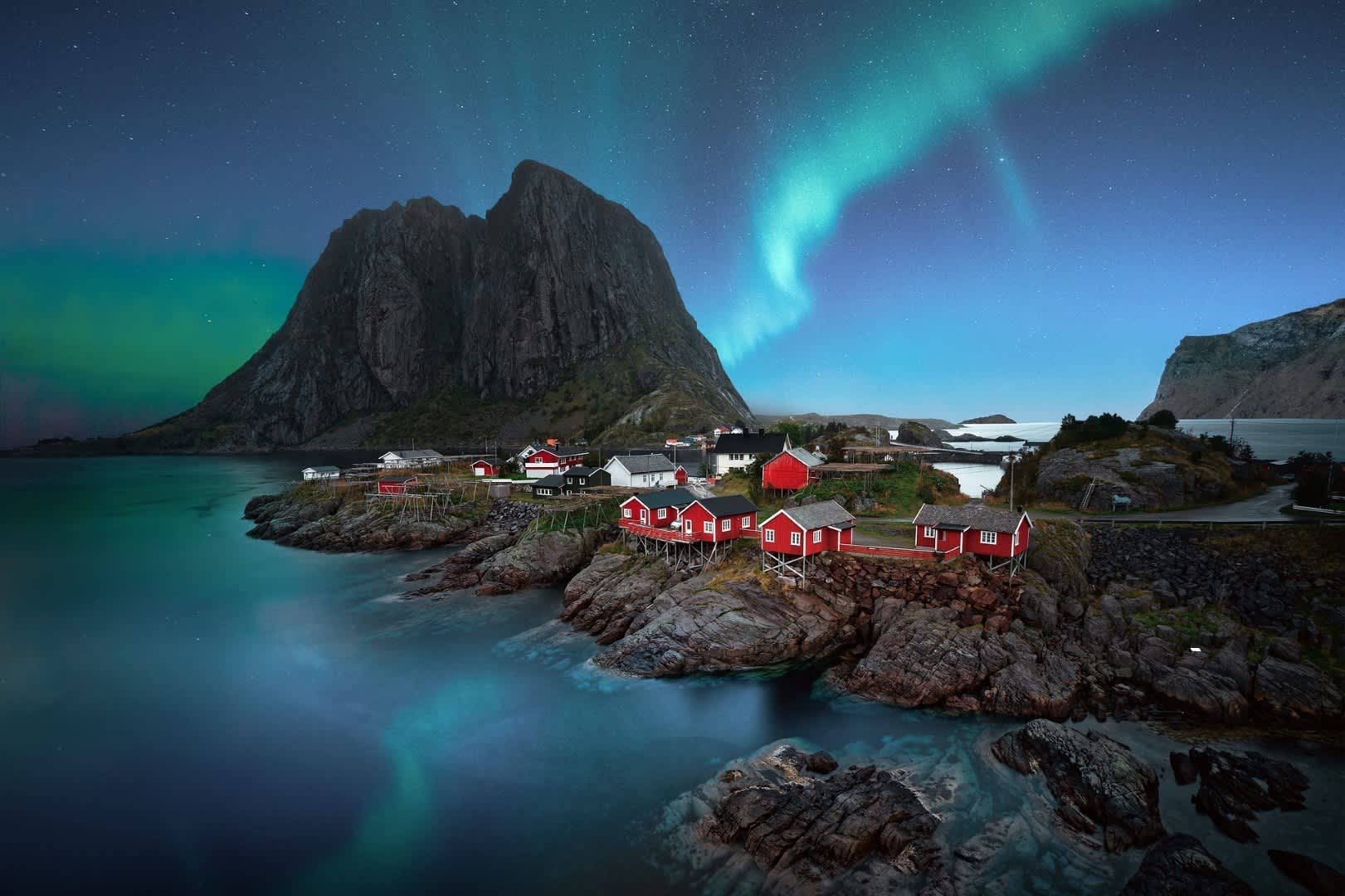 The northern lights are shining over a small village on a rocky island.