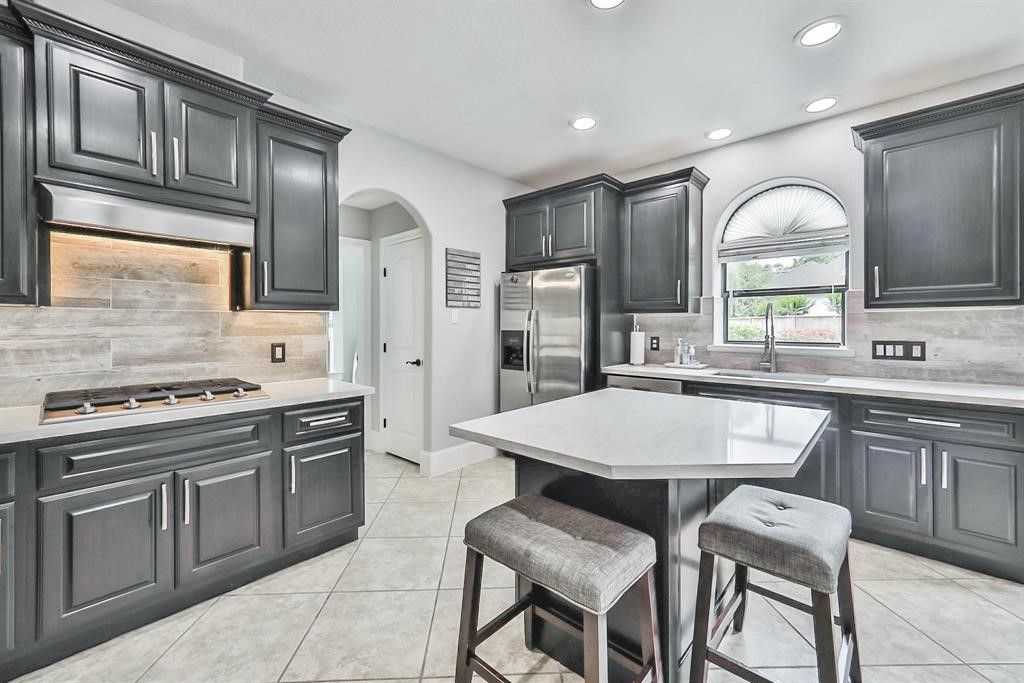 Dark gray kitchen with white countertops and island. Two stools are at the island.