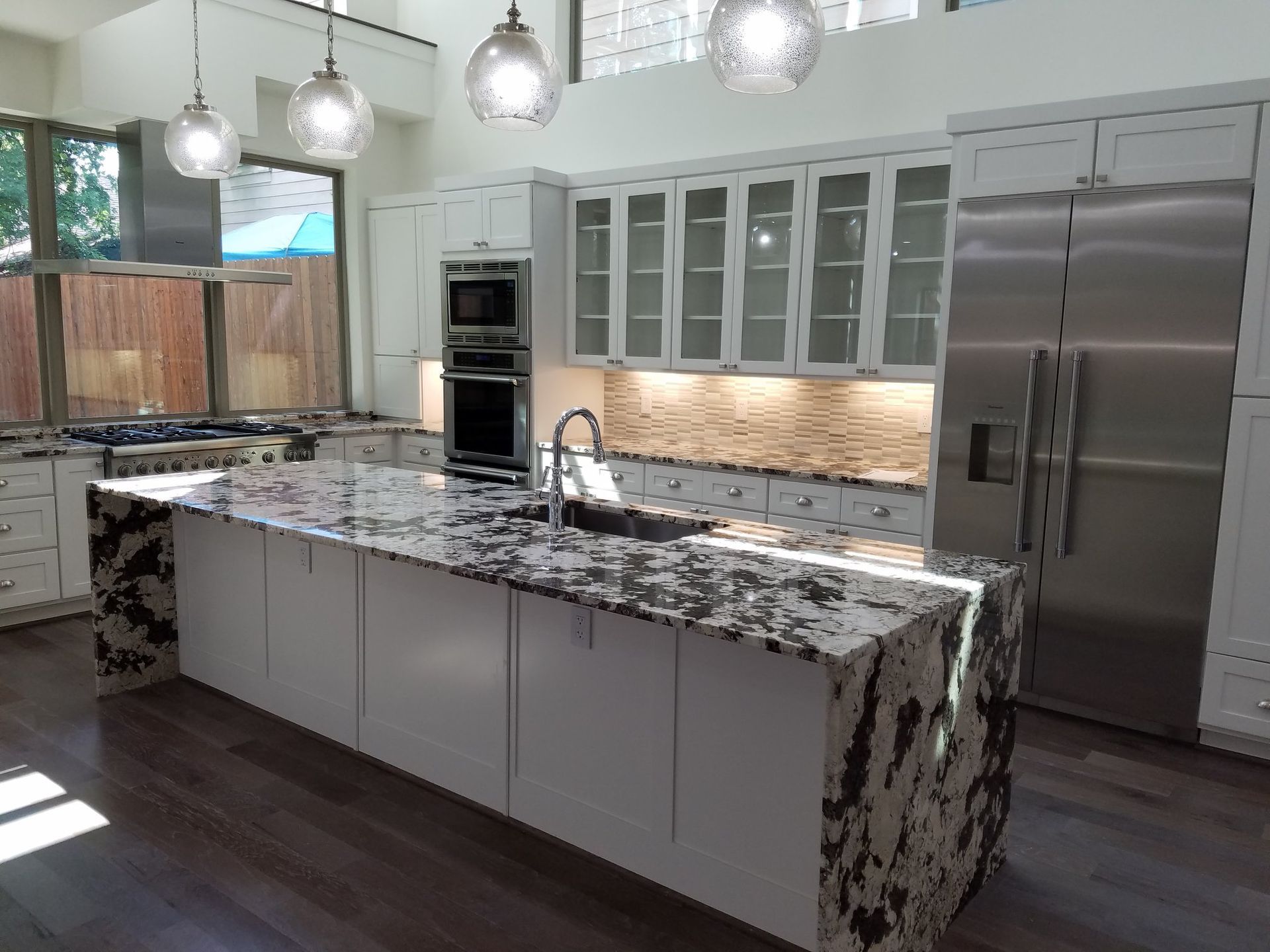 Modern kitchen with white cabinets, granite island, stainless steel appliances, and pendant lights.