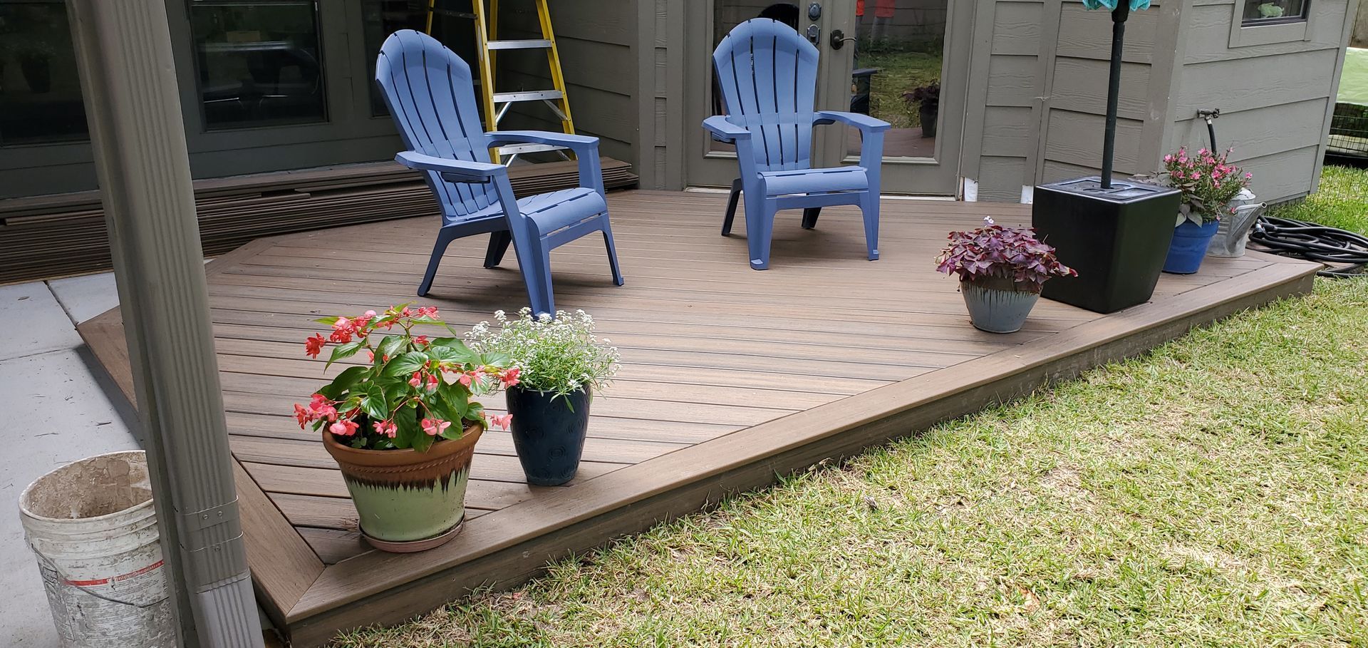 Patio with blue chairs, potted flowers, and green grass.
