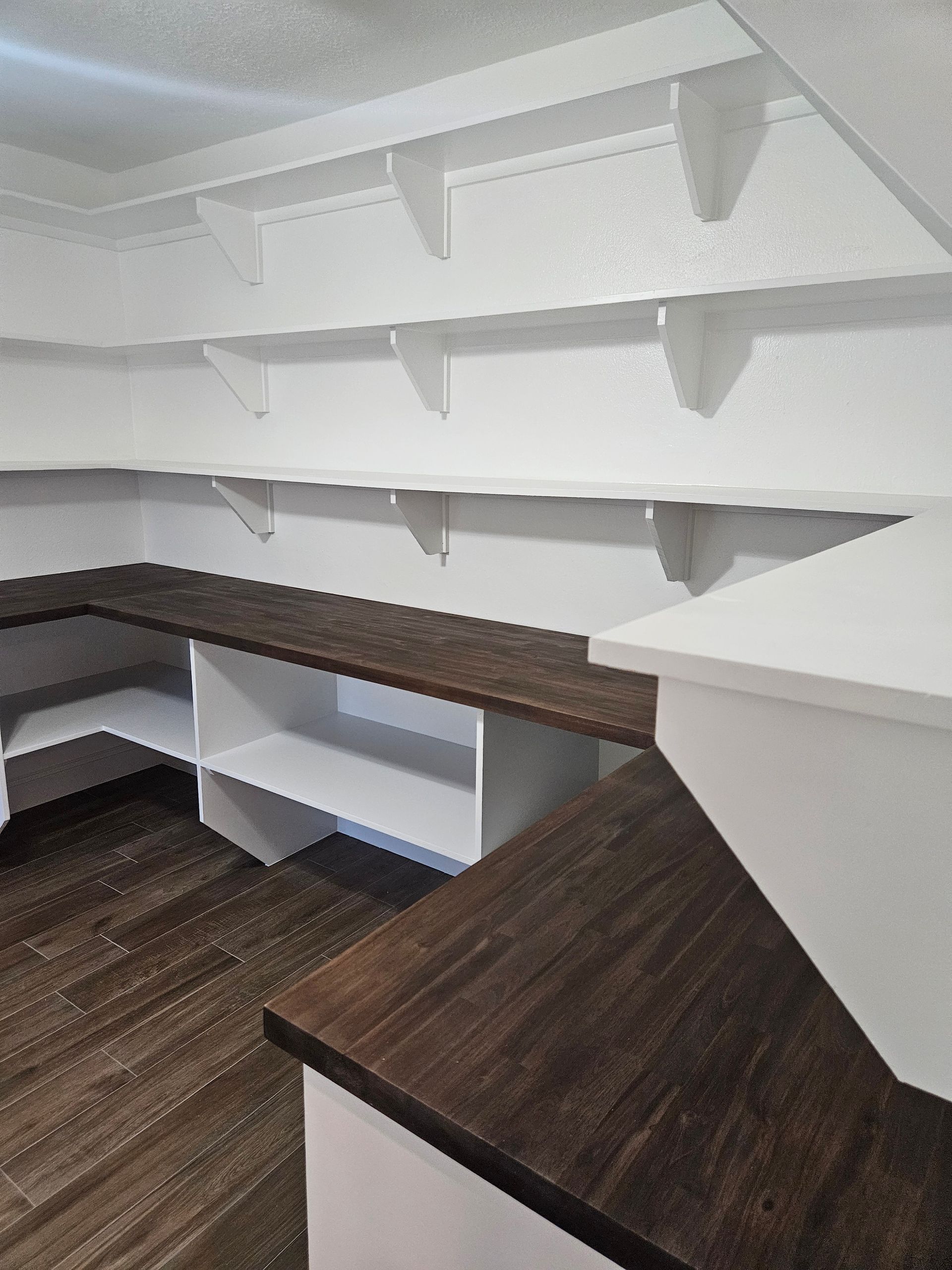 White pantry with dark wood countertops and shelves.