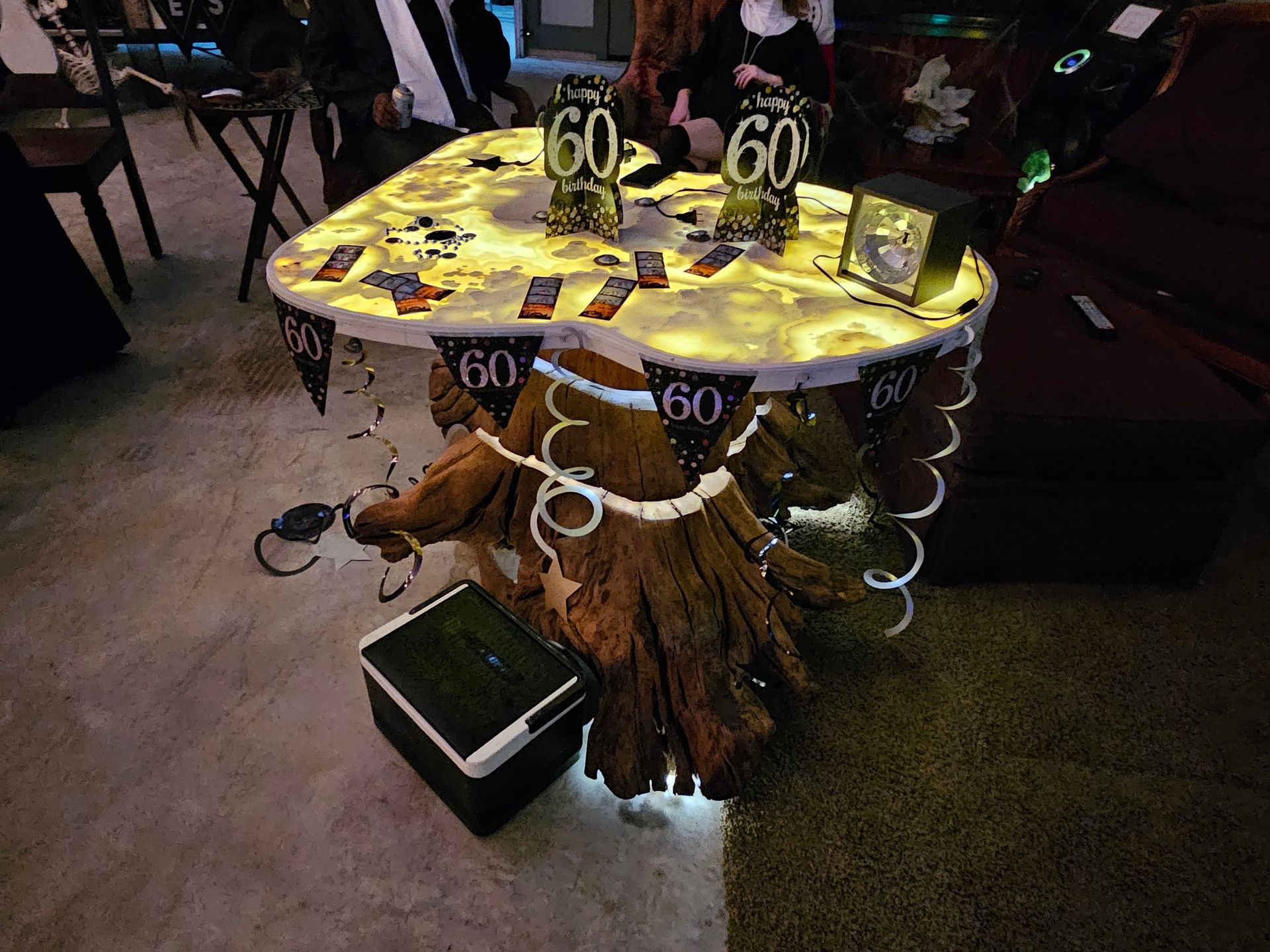 A 60th birthday table with an illuminated top and a root base. Decor includes flags and candles.