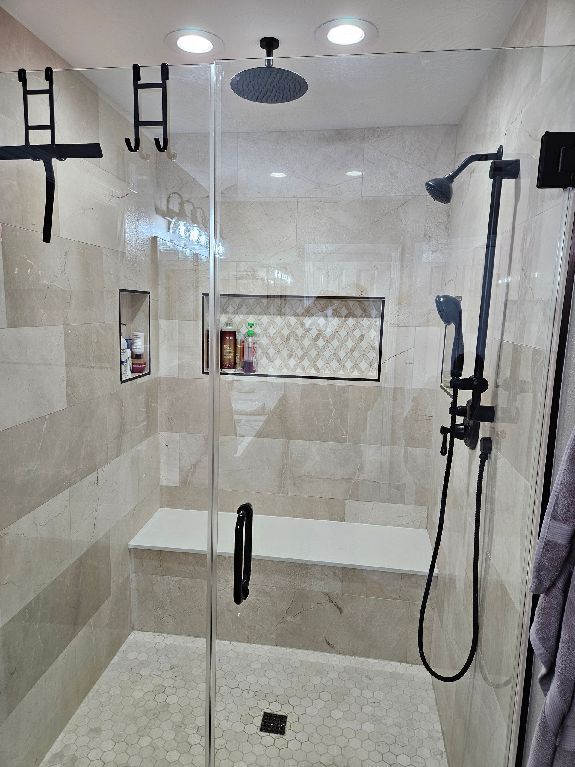 Bathroom with glass shower door, tiled walls, bench, and black shower fixtures.