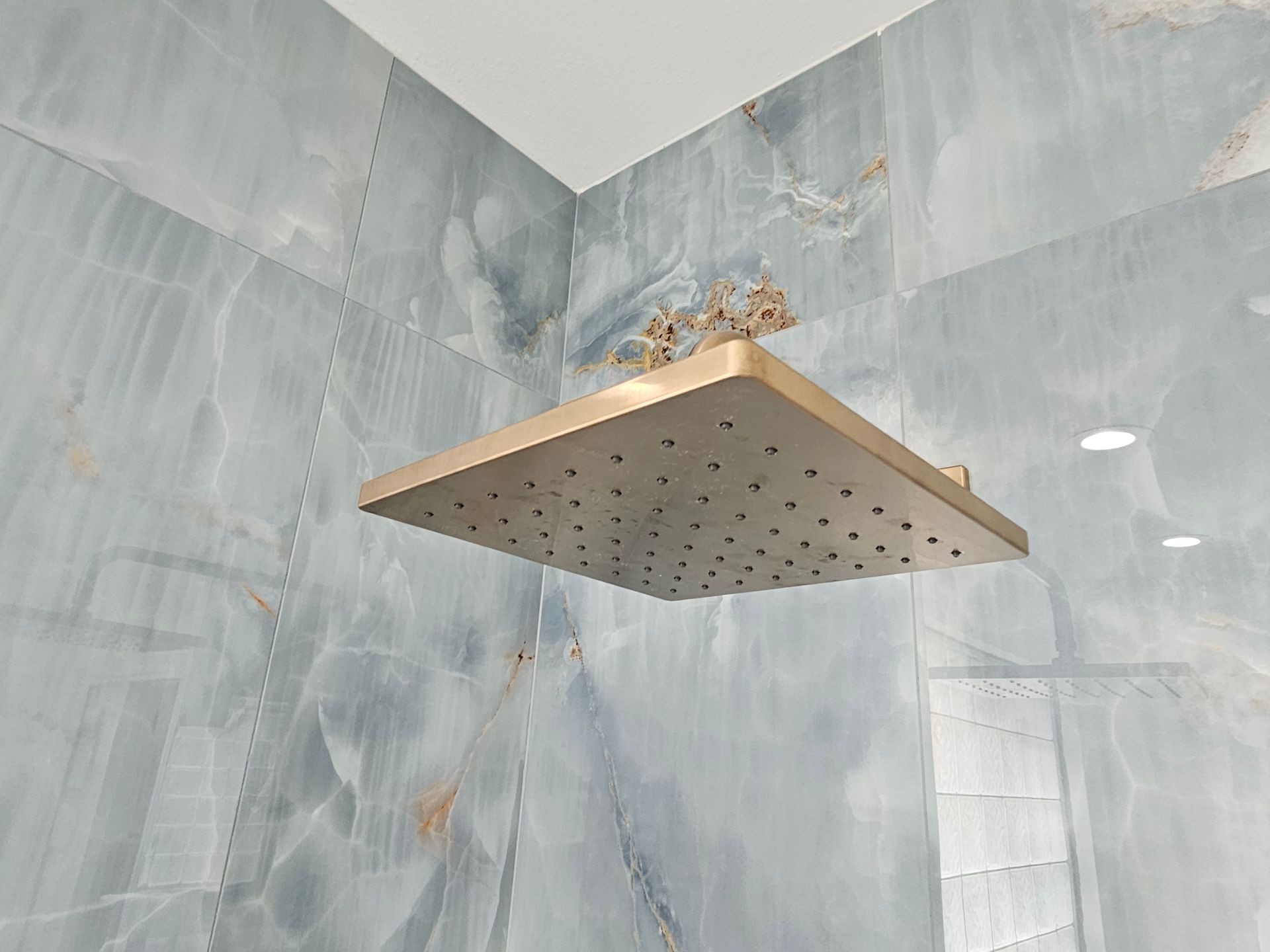 Square gold showerhead in a blue-tiled shower.
