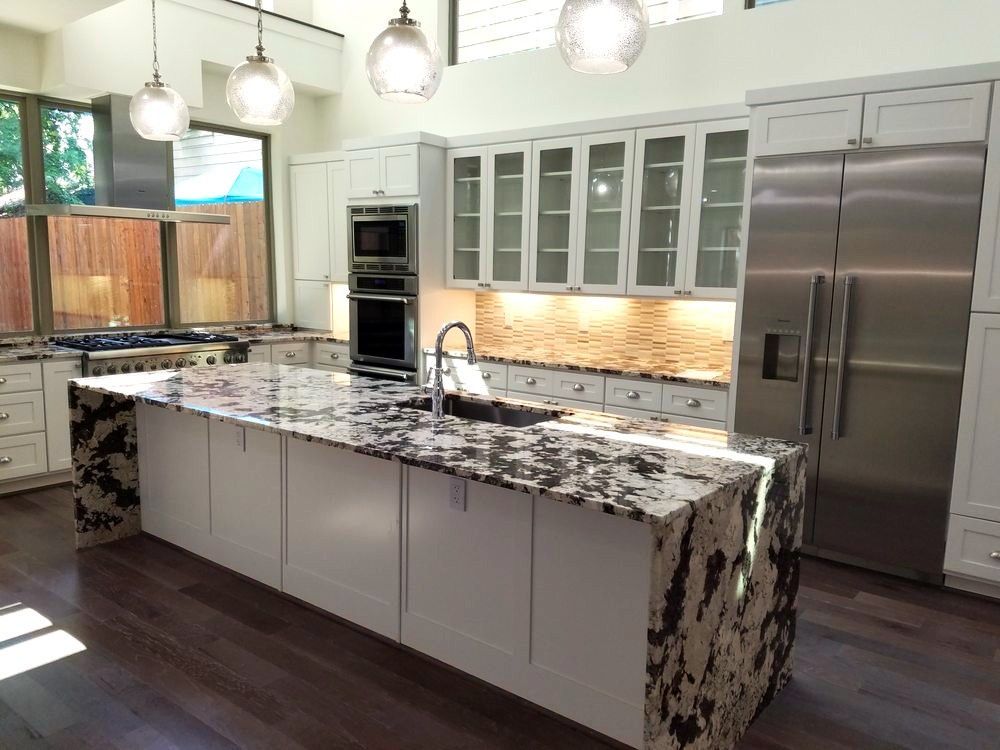 Modern kitchen with white cabinets, granite island, stainless steel appliances, and pendant lights.