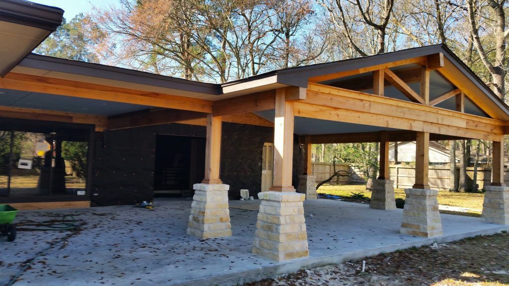 A covered outdoor area under construction with wooden beams, stone pillars, and a concrete floor.