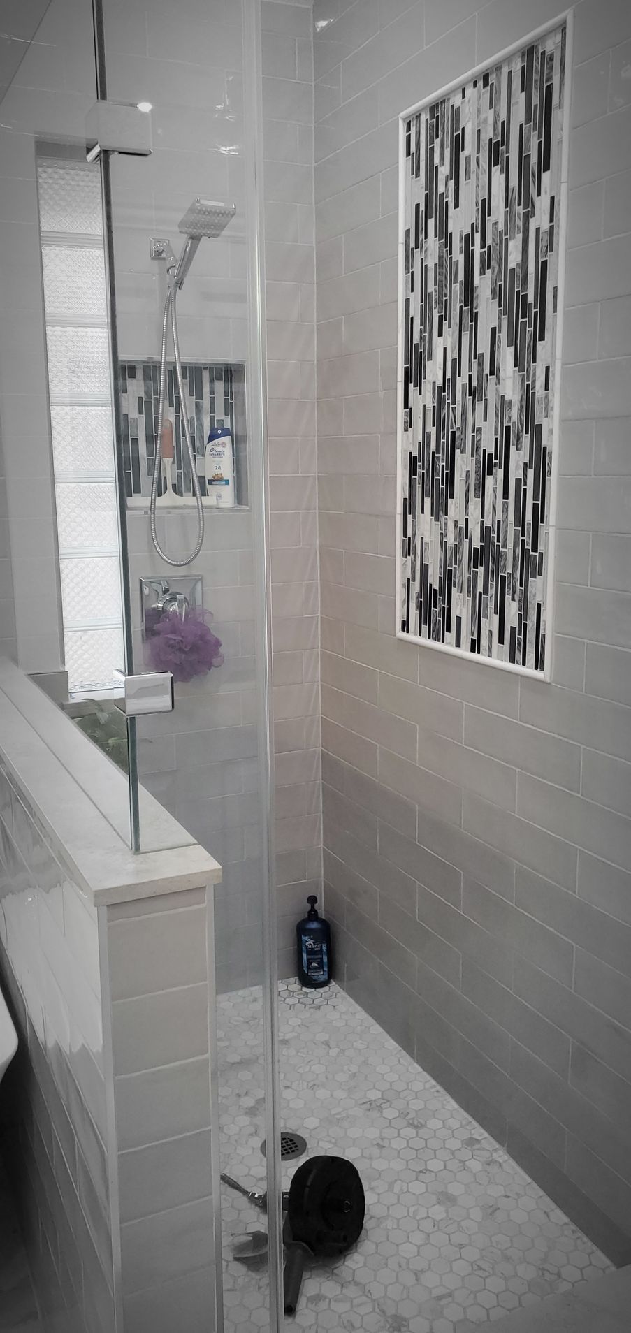 A modern shower with gray tiles, glass door, and black and white art.