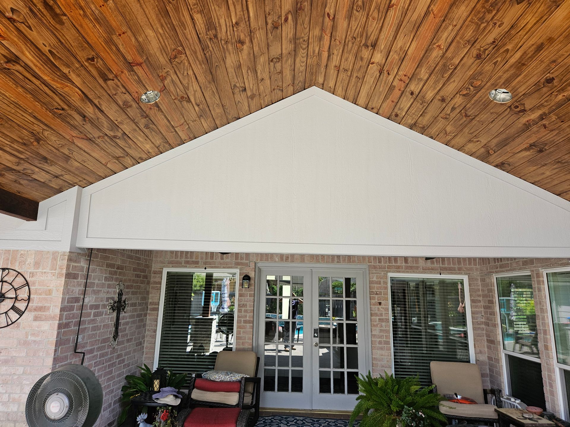 Brick patio with wood ceiling and white gable over double doors and windows.