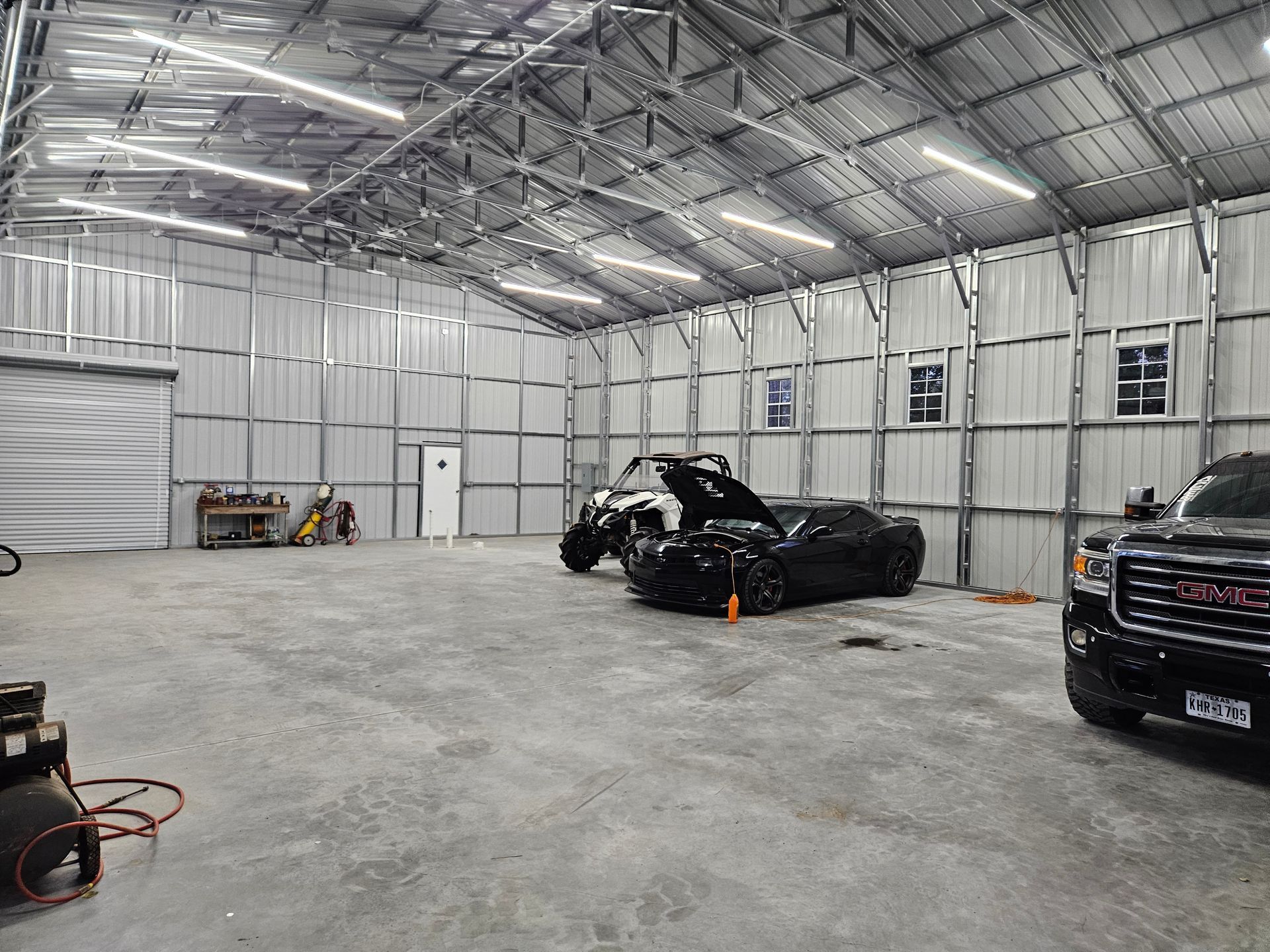 Inside a large, metal garage with a black car, a white vehicle, and a truck.