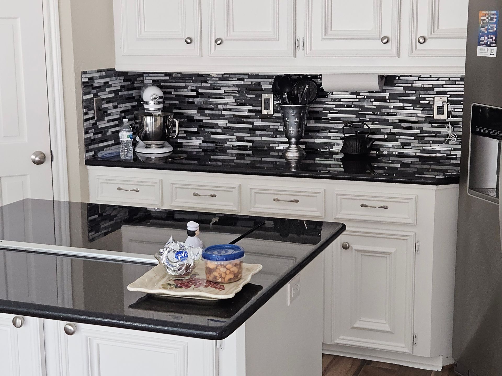 Kitchen with white cabinets, black countertops, and a black and white tile backsplash. A kitchen island is in the foreground.