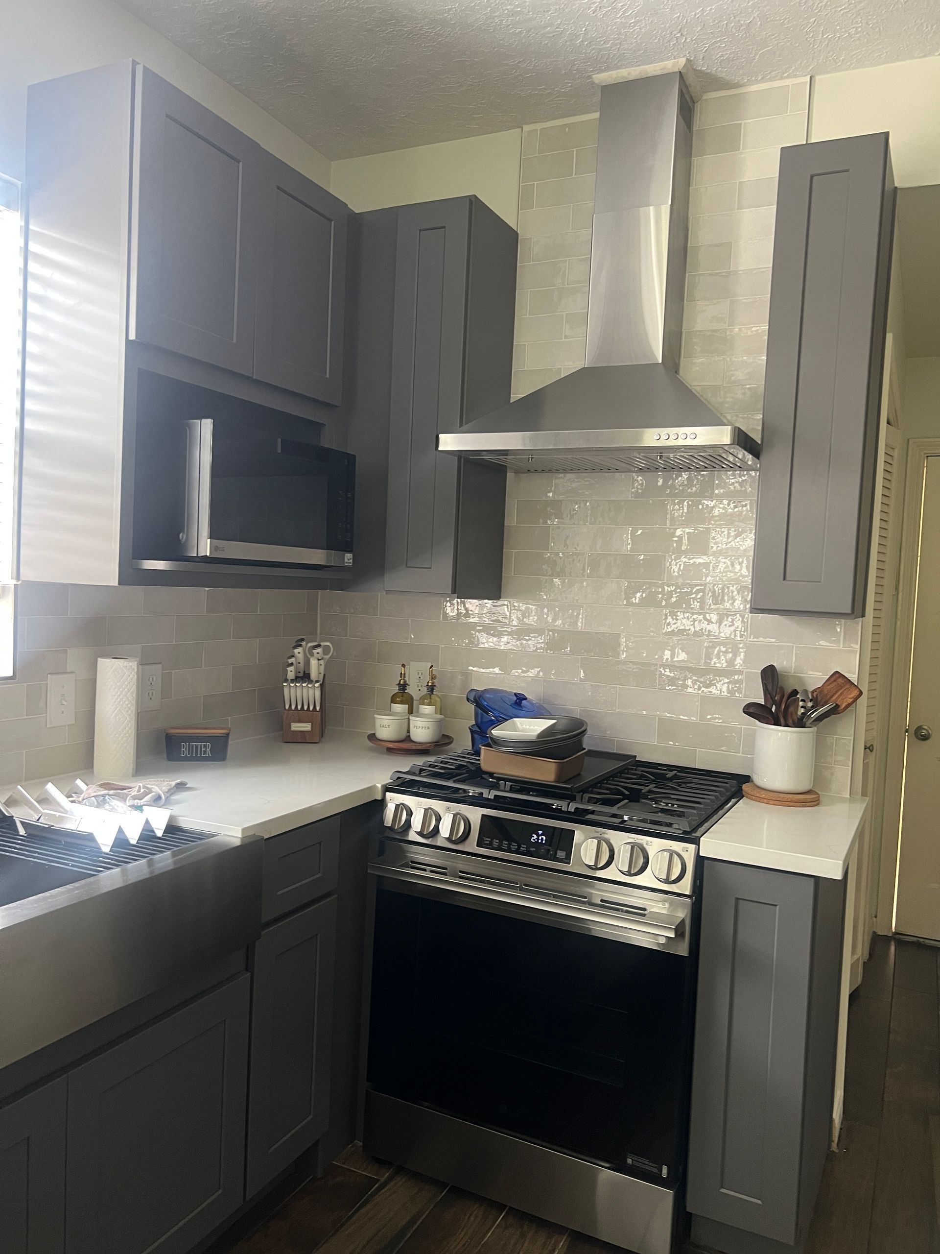 Gray kitchen with stainless steel appliances, gray cabinets, and light-colored backsplash.