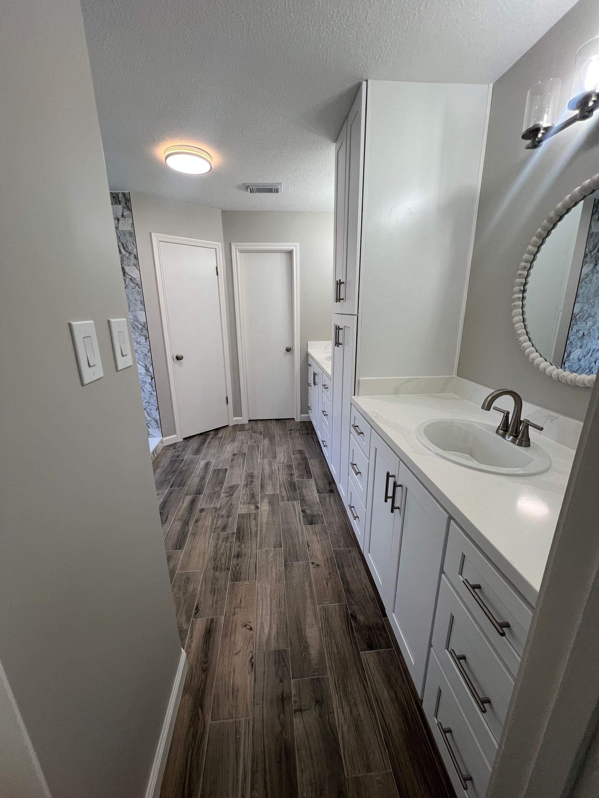 Bathroom with white cabinets, a sink, a mirror, and wood-look flooring.