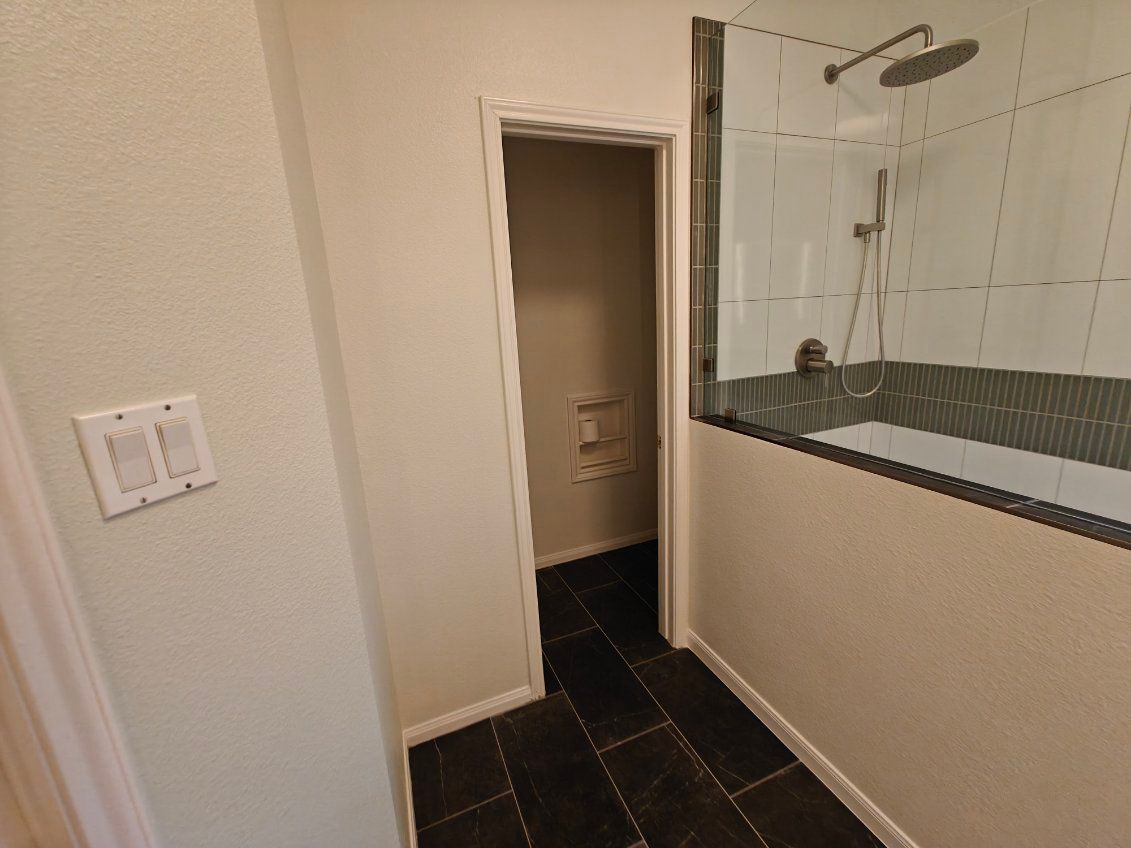 Bathroom interior with shower, dark tile floor, and a doorway.