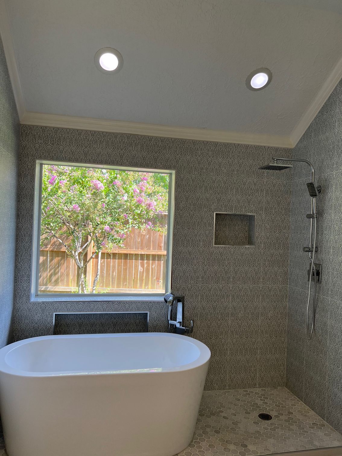 Modern bathroom with freestanding tub, shower, window, and mosaic tile walls, lit by recessed lights.